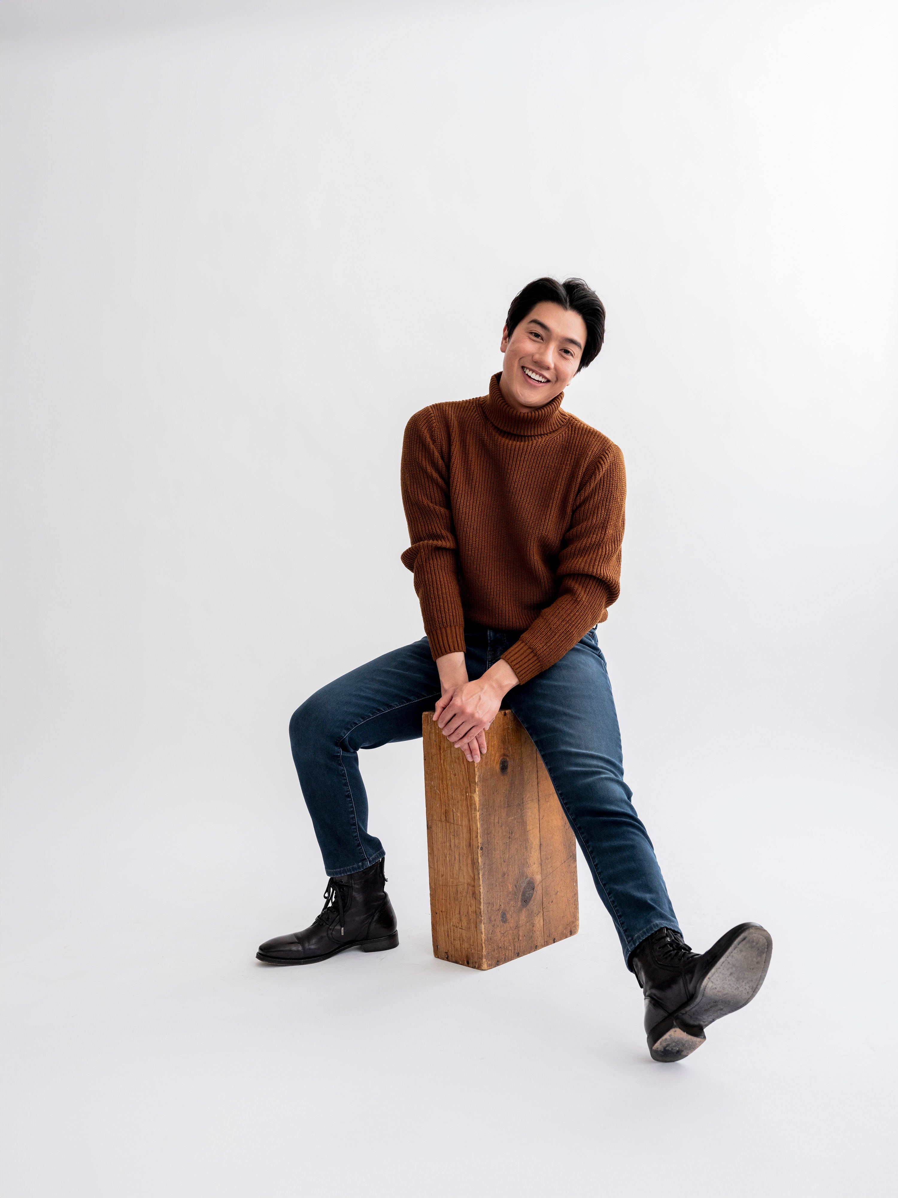 Man in white room sitting on apple box smiling to camera