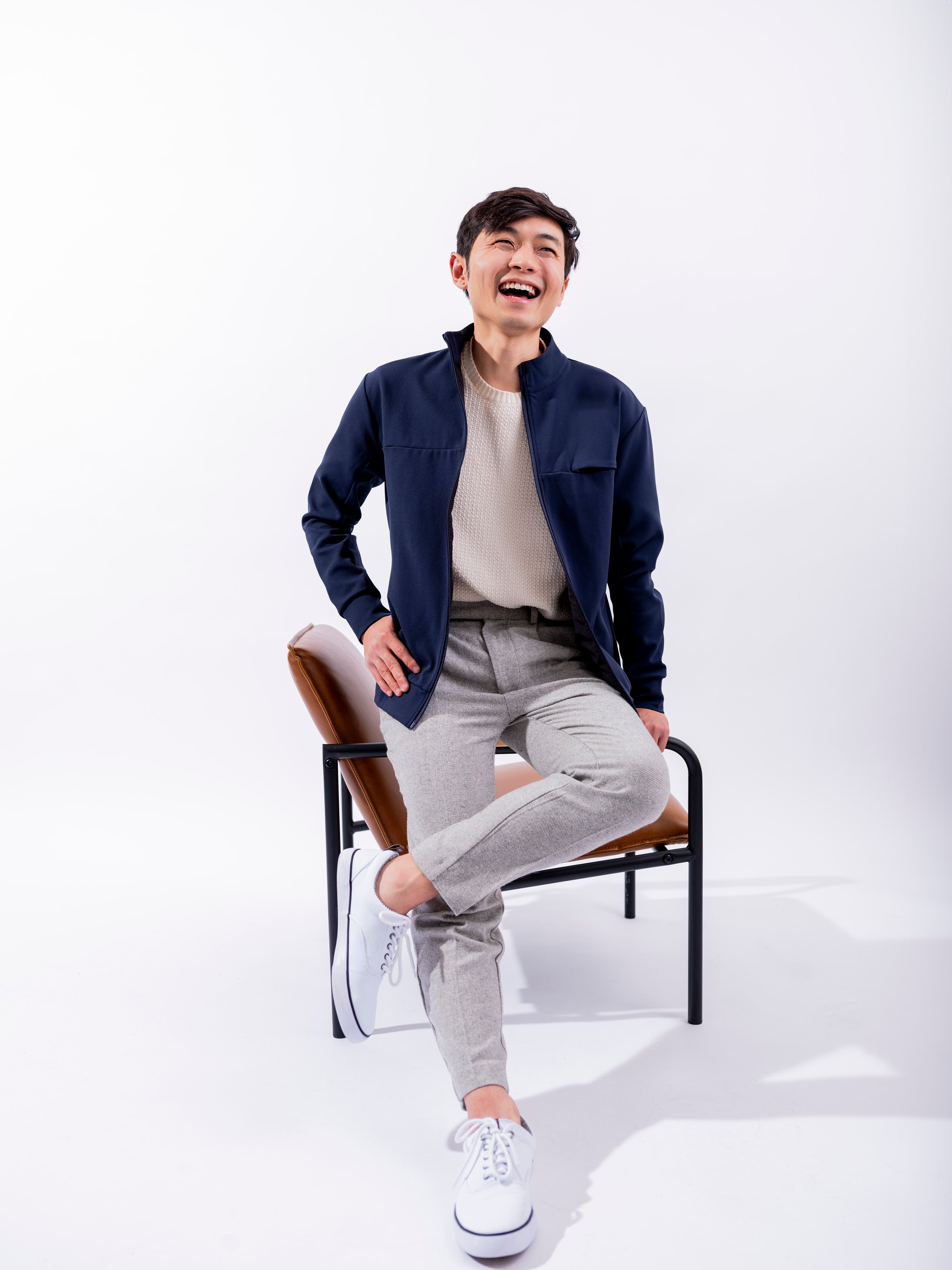 Man in white room sitting on chair smiling wearing Hunter Jacket in Cobalt Navy