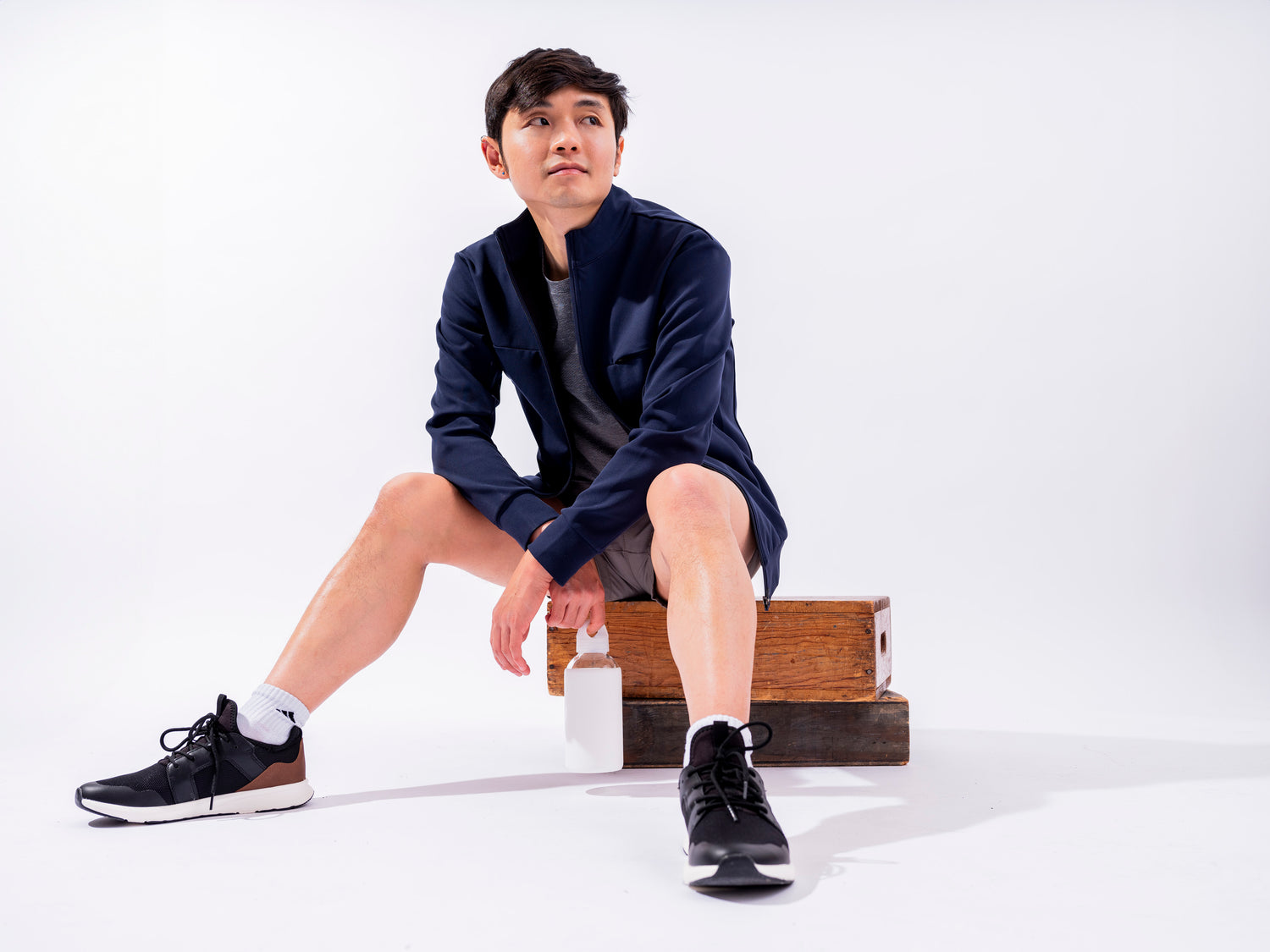 Man sitting in white room on apple boxes in activewear and Hunter Jacket